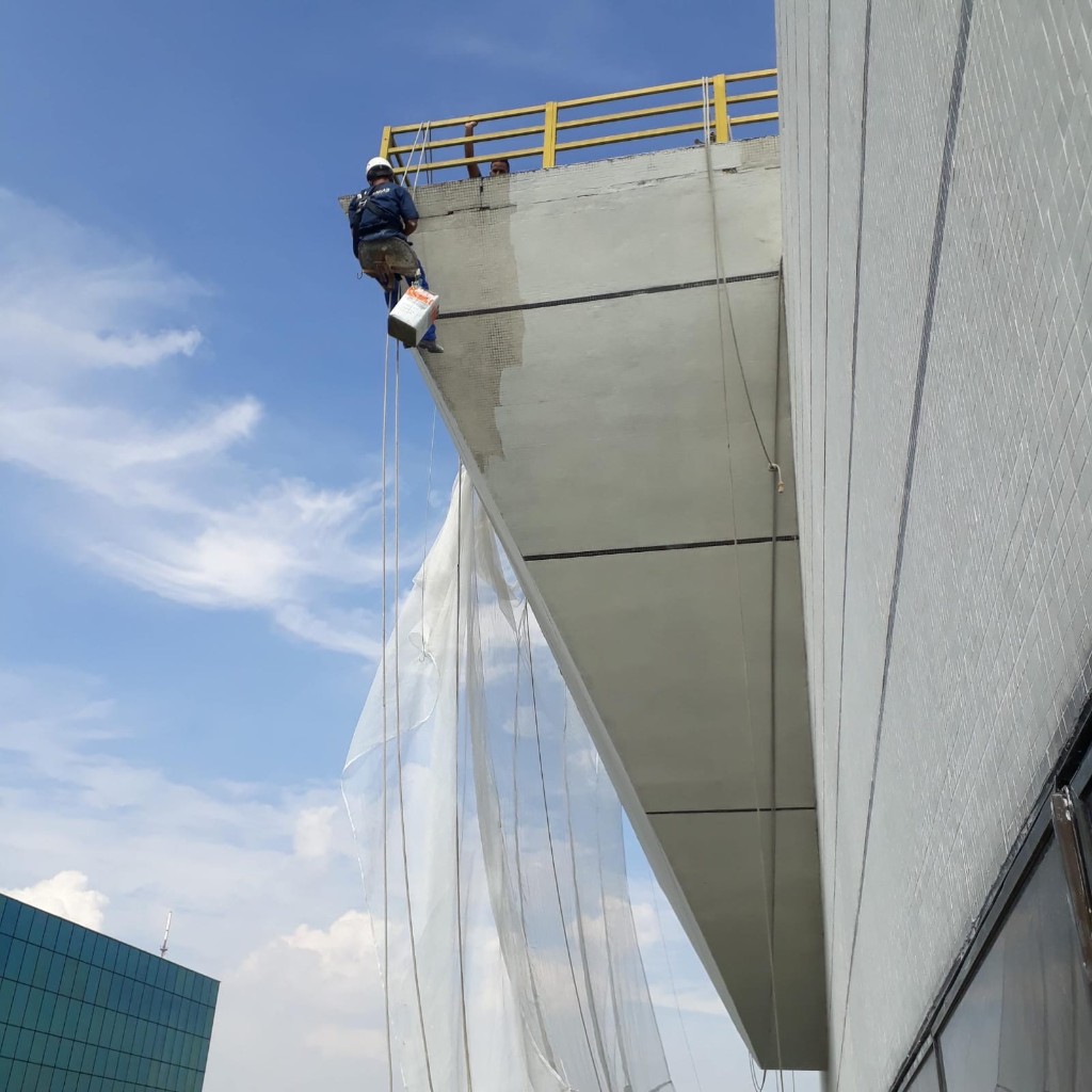 Profissional fazendo pintura em altura na fachada de um prédio